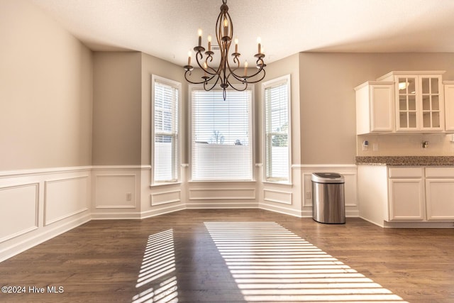 unfurnished dining area with dark hardwood / wood-style floors, a healthy amount of sunlight, a textured ceiling, and a chandelier