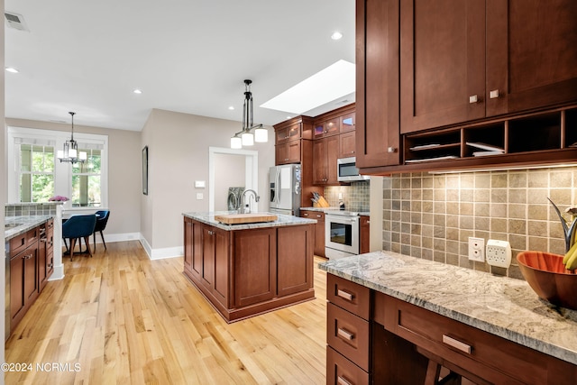 kitchen featuring backsplash, light stone countertops, stainless steel appliances, light wood-type flooring, and decorative light fixtures