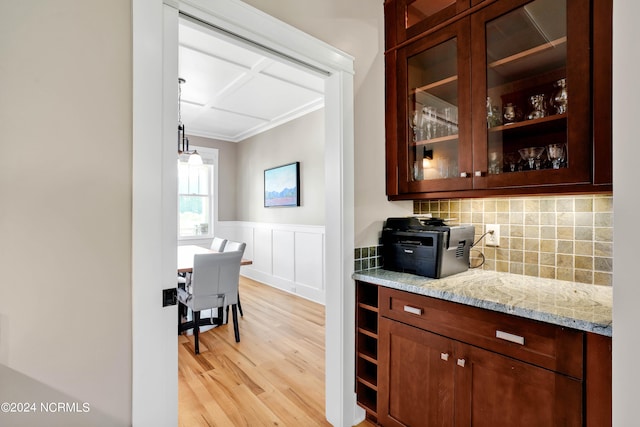 bar with light stone countertops, light hardwood / wood-style flooring, ornamental molding, and tasteful backsplash