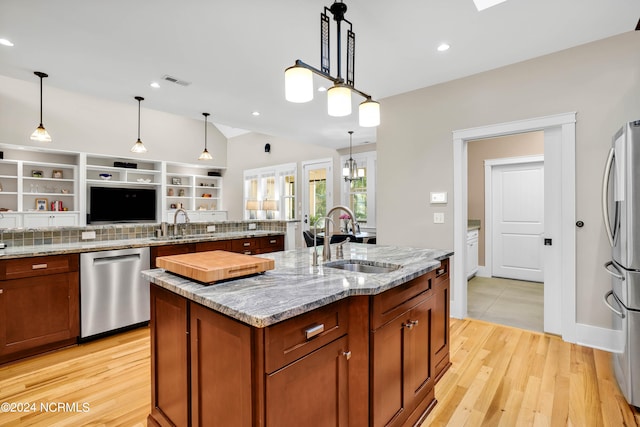 kitchen with sink, decorative light fixtures, a kitchen island with sink, appliances with stainless steel finishes, and light wood-type flooring