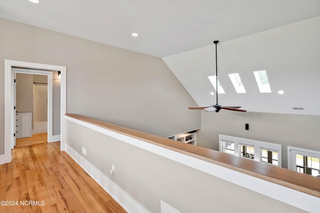 corridor featuring light wood-type flooring, a skylight, and high vaulted ceiling