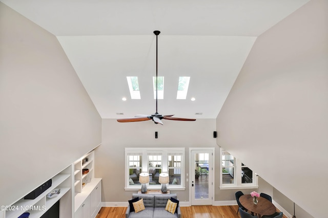 living room featuring ceiling fan, vaulted ceiling with skylight, and light hardwood / wood-style floors