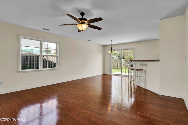 unfurnished living room featuring ceiling fan with notable chandelier and dark wood-type flooring