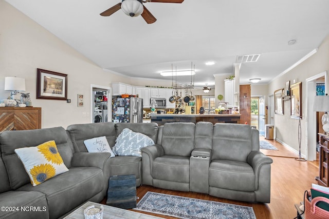 living room with ornamental molding, ceiling fan, washer / dryer, lofted ceiling, and light wood-type flooring