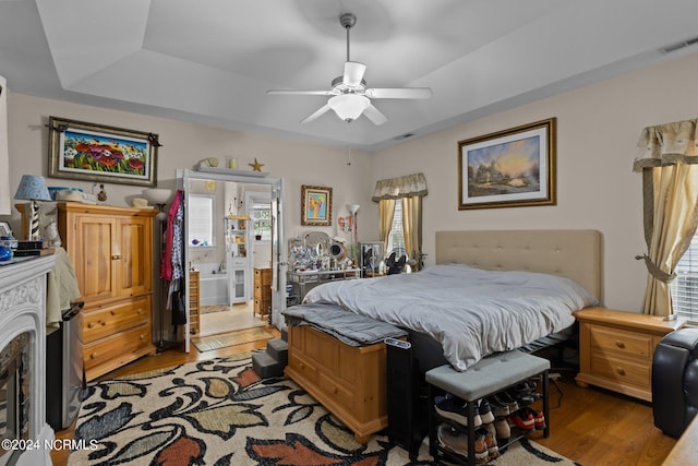 bedroom featuring light wood-type flooring, a raised ceiling, ceiling fan, and ensuite bathroom