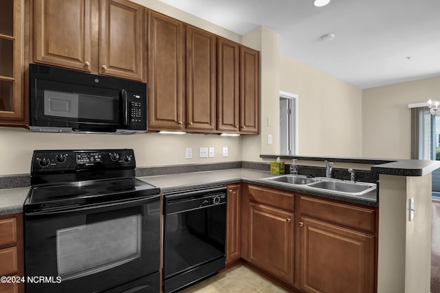 kitchen featuring dark countertops, brown cabinets, a sink, black appliances, and a peninsula