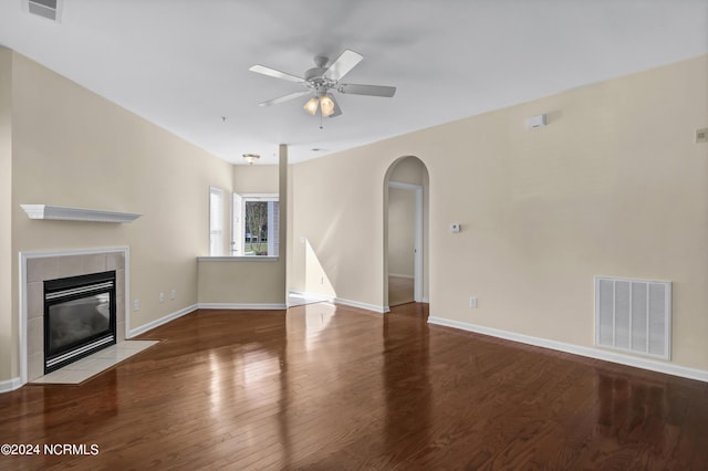 unfurnished living room featuring a tiled fireplace, arched walkways, wood finished floors, and visible vents