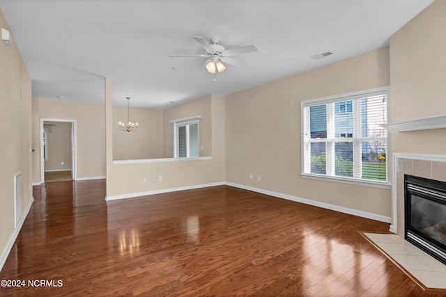 unfurnished living room with a tile fireplace, ceiling fan with notable chandelier, and dark hardwood / wood-style floors