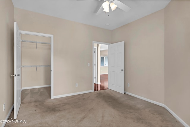 unfurnished bedroom featuring a walk in closet, light carpet, a closet, and ceiling fan