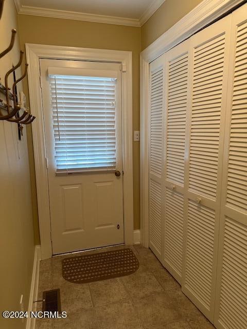 doorway with ornamental molding and light tile patterned floors