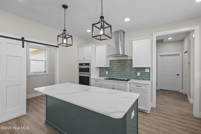 kitchen featuring pendant lighting, backsplash, white cabinets, wall chimney exhaust hood, and a barn door