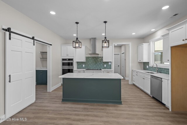 kitchen with appliances with stainless steel finishes, wall chimney exhaust hood, a barn door, decorative light fixtures, and a center island