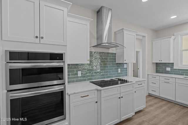 kitchen featuring wall chimney range hood, black electric cooktop, double oven, light stone counters, and white cabinetry