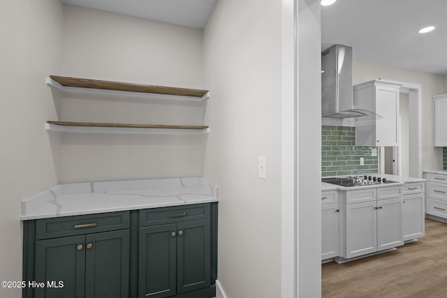 kitchen with light stone countertops, white cabinetry, wall chimney exhaust hood, light hardwood / wood-style floors, and black electric cooktop