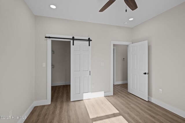 unfurnished bedroom featuring a walk in closet, hardwood / wood-style floors, a barn door, and ceiling fan