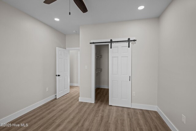 unfurnished bedroom featuring ceiling fan, a barn door, light wood-type flooring, a spacious closet, and a closet