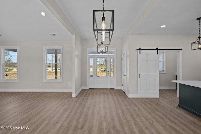 entryway with a barn door, an inviting chandelier, and light wood-type flooring