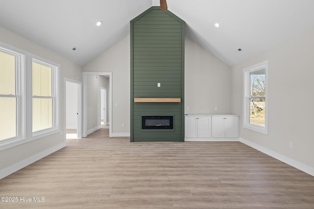 unfurnished living room with lofted ceiling, a large fireplace, and light hardwood / wood-style floors