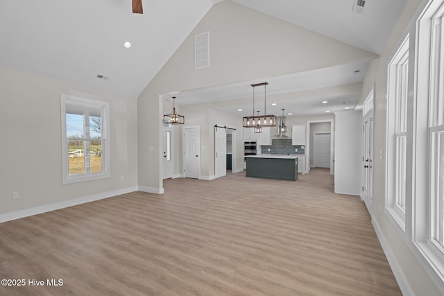 unfurnished living room with a barn door, ceiling fan, high vaulted ceiling, and light wood-type flooring