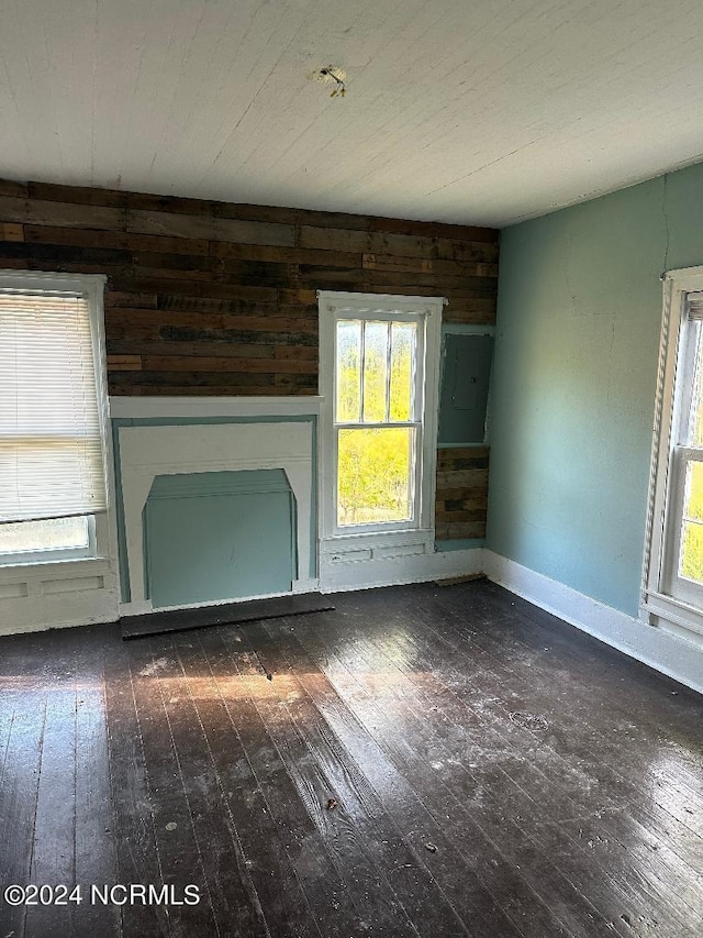 unfurnished living room featuring electric panel, wood walls, and dark hardwood / wood-style floors