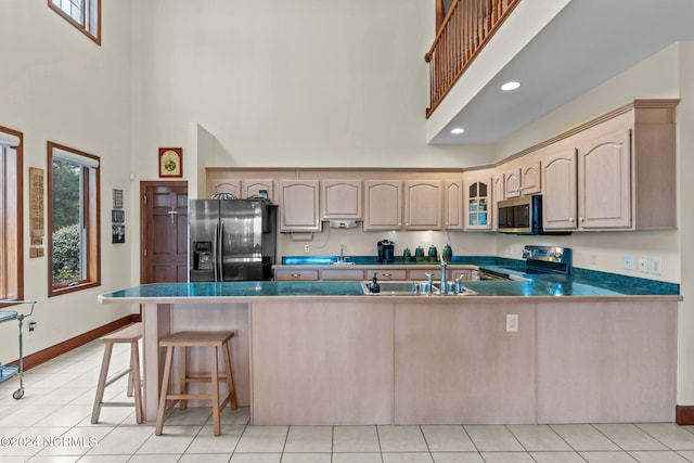 kitchen with light brown cabinetry, light tile patterned floors, appliances with stainless steel finishes, and kitchen peninsula