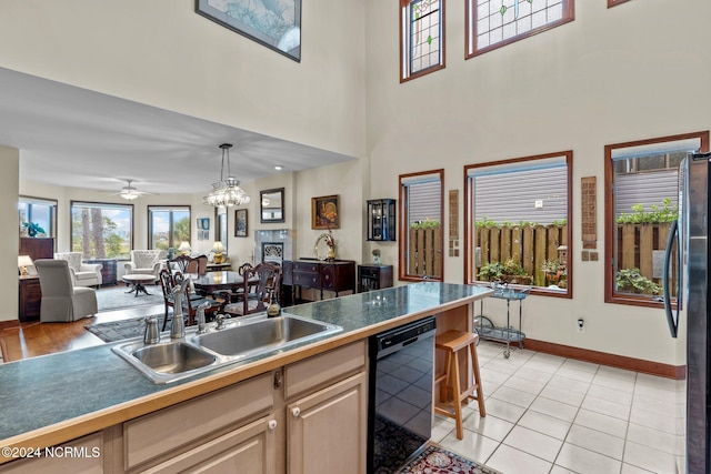 kitchen featuring pendant lighting, stainless steel fridge, light tile patterned floors, black dishwasher, and ceiling fan with notable chandelier