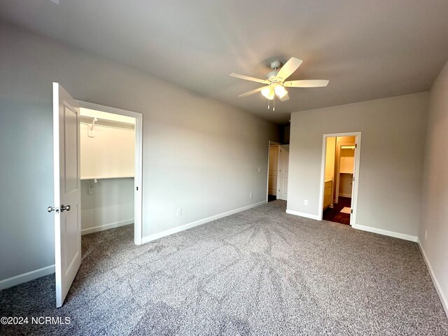 unfurnished bedroom with a spacious closet, dark carpet, ceiling fan, and a closet