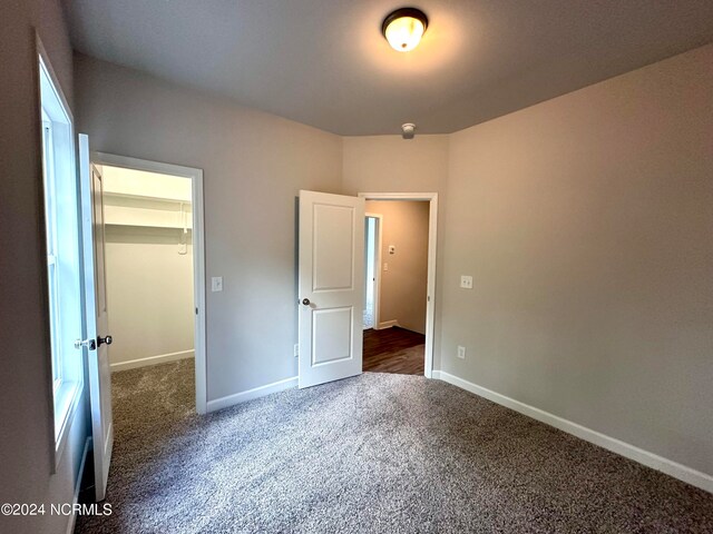 unfurnished bedroom with dark colored carpet, a walk in closet, and a closet