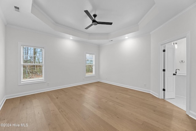 empty room with light hardwood / wood-style floors, a raised ceiling, ceiling fan, and ornamental molding