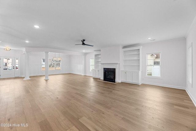 unfurnished living room featuring light wood-type flooring, decorative columns, ceiling fan with notable chandelier, crown molding, and built in features