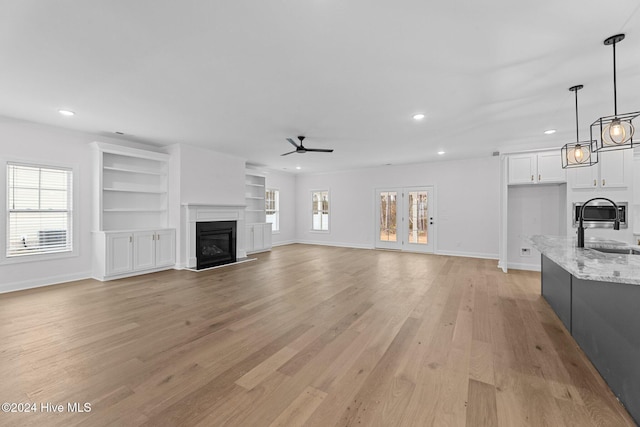 unfurnished living room featuring built in shelves, light hardwood / wood-style floors, ceiling fan, and sink