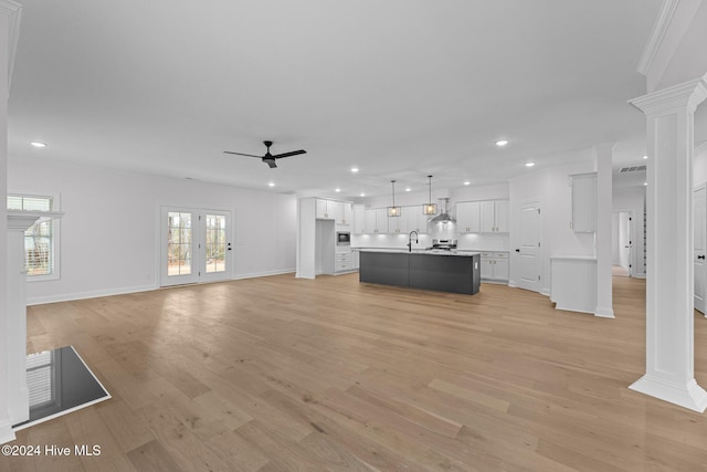 unfurnished living room featuring sink, ceiling fan, ornate columns, ornamental molding, and light hardwood / wood-style floors