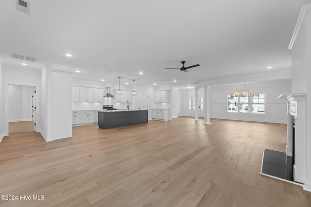 unfurnished living room featuring light wood-type flooring, ceiling fan with notable chandelier, ornamental molding, and sink