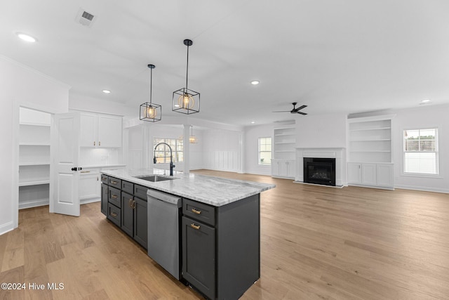 kitchen featuring stainless steel dishwasher, sink, decorative light fixtures, a center island with sink, and white cabinets