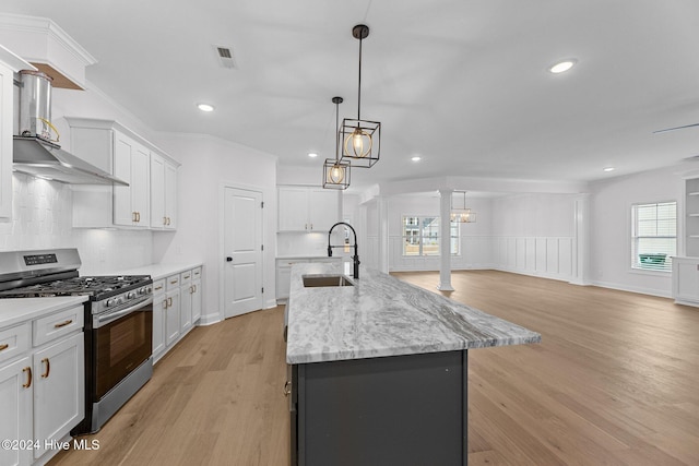 kitchen with gas stove, sink, hanging light fixtures, an island with sink, and white cabinets