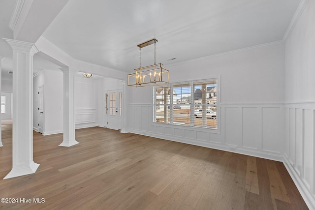 unfurnished dining area featuring light hardwood / wood-style flooring, an inviting chandelier, crown molding, and ornate columns