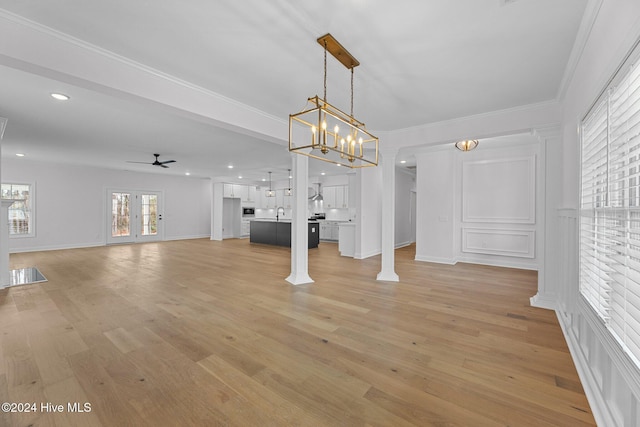 interior space featuring french doors, ceiling fan with notable chandelier, crown molding, light hardwood / wood-style flooring, and decorative columns