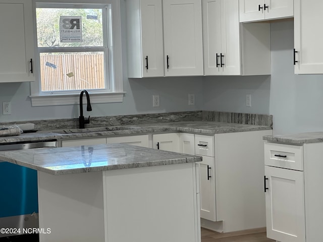 kitchen with a kitchen island, sink, light stone counters, and white cabinets