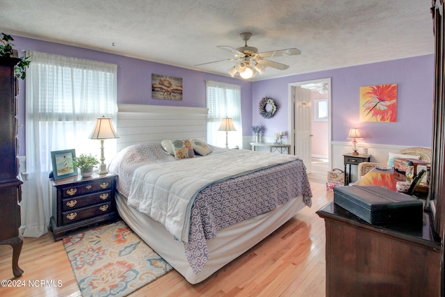 bedroom with a textured ceiling, hardwood / wood-style flooring, connected bathroom, and ceiling fan