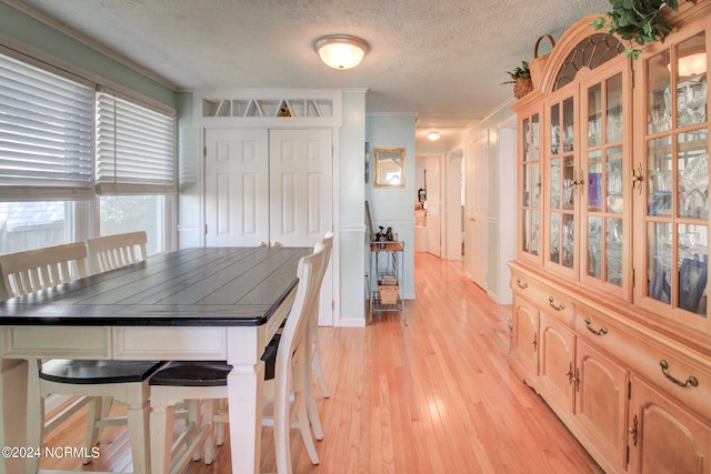 dining space with light hardwood / wood-style flooring, a textured ceiling, and crown molding