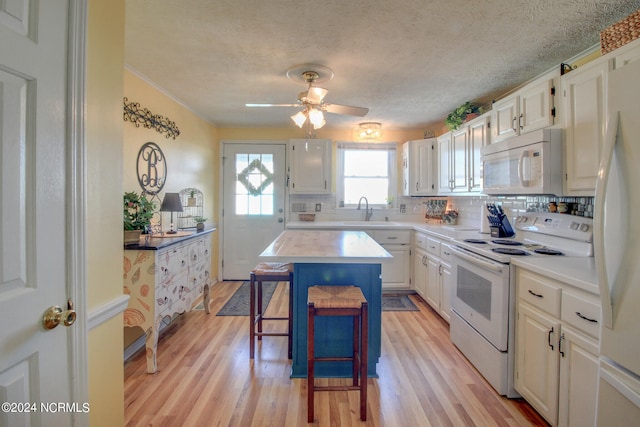 kitchen with a breakfast bar area, light hardwood / wood-style flooring, a center island, white cabinets, and white appliances