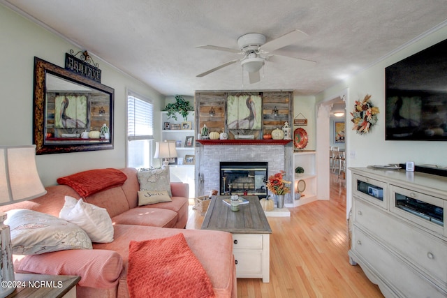 living room with ceiling fan, a textured ceiling, light wood-type flooring, ornamental molding, and a fireplace