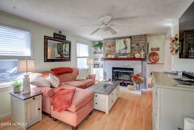 living room featuring ceiling fan, a textured ceiling, light hardwood / wood-style flooring, a fireplace, and crown molding