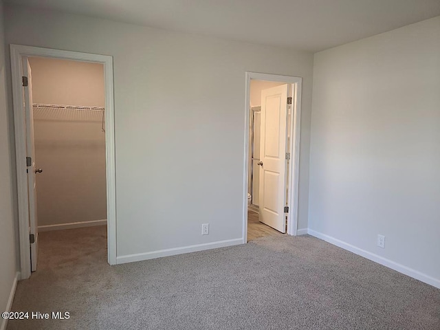 unfurnished bedroom featuring a walk in closet, light colored carpet, and a closet