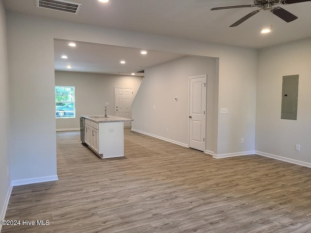 kitchen with white cabinetry, light stone counters, electric panel, an island with sink, and light hardwood / wood-style floors