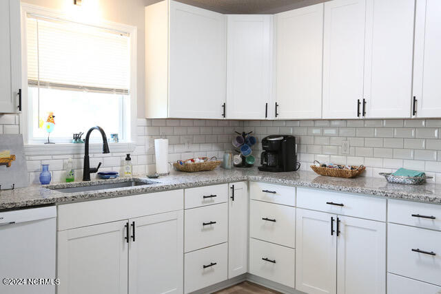 kitchen featuring decorative backsplash, light stone counters, white cabinets, white dishwasher, and sink