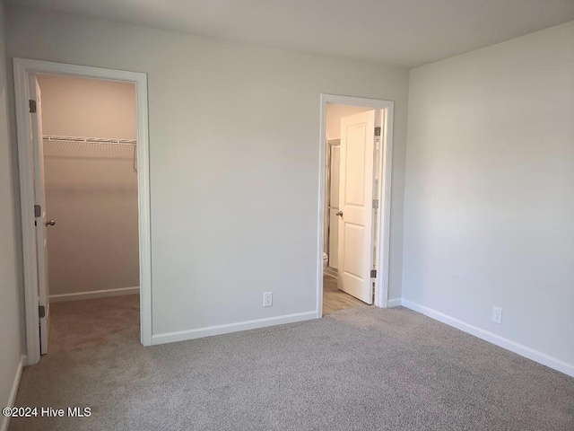 unfurnished bedroom with a walk in closet, light colored carpet, and a closet