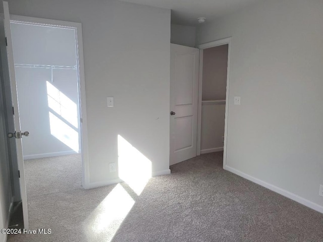 unfurnished bedroom with light carpet, a closet, and a spacious closet