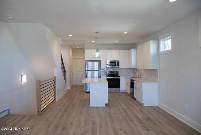 kitchen with pendant lighting, sink, appliances with stainless steel finishes, a kitchen island, and white cabinetry