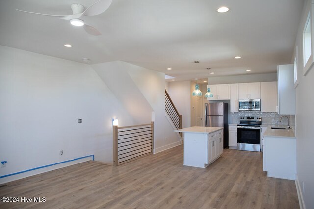 kitchen with white cabinets, a kitchen island, stainless steel appliances, and hanging light fixtures